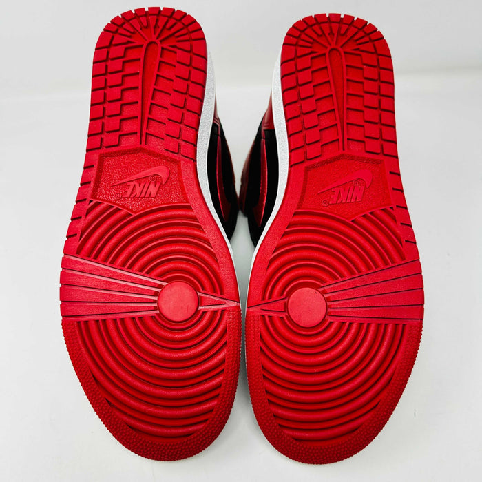 A Jordan 1 Retro High 85 OG Bred (2025) sneaker by Jordan sits on its matching shoebox, showcasing the iconic swoosh and Air Jordan logo. Its styled in black and red with a white midsole, bold red laces, and detailed black accents.