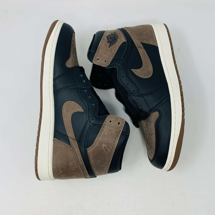 The Jordan 1 Retro High OG Palomino, a new black and brown sneaker from the Jordan brand, is displayed atop a pristine black and yellow Nike shoebox. The 2023 high-top design features the signature swoosh and Air Jordan logo, emphasizing its fresh-off-the-shelf allure.