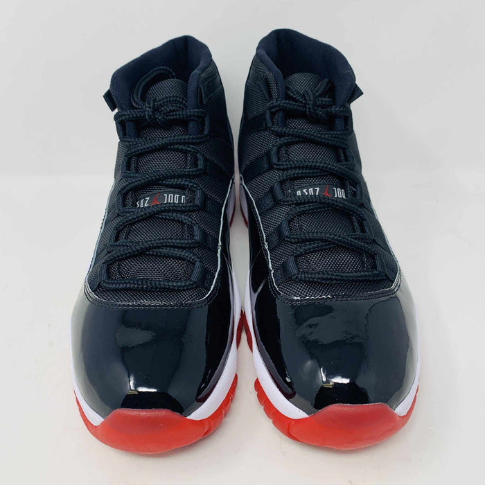 The brand new Jordan 11 Bred 2019 features a black and red high-top design with glossy accents, striking red soles, and a bold red Jumpman logo. It sits atop an orange and black Nike shoebox, exuding style and performance.