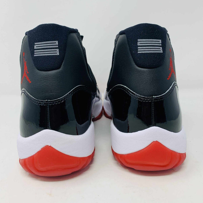 The brand new Jordan 11 Bred 2019 features a black and red high-top design with glossy accents, striking red soles, and a bold red Jumpman logo. It sits atop an orange and black Nike shoebox, exuding style and performance.