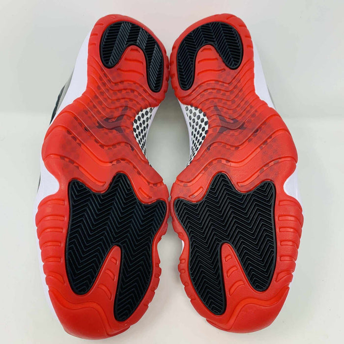 The brand new Jordan 11 Bred 2019 features a black and red high-top design with glossy accents, striking red soles, and a bold red Jumpman logo. It sits atop an orange and black Nike shoebox, exuding style and performance.
