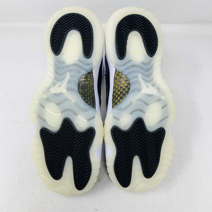 A pair of authentic Jordan 11 Retro DMP Gratitude (2023) (GS) sneakers, featuring a glossy white and black finish with a gold logo, is placed on top of a gray Nike Air shoebox.