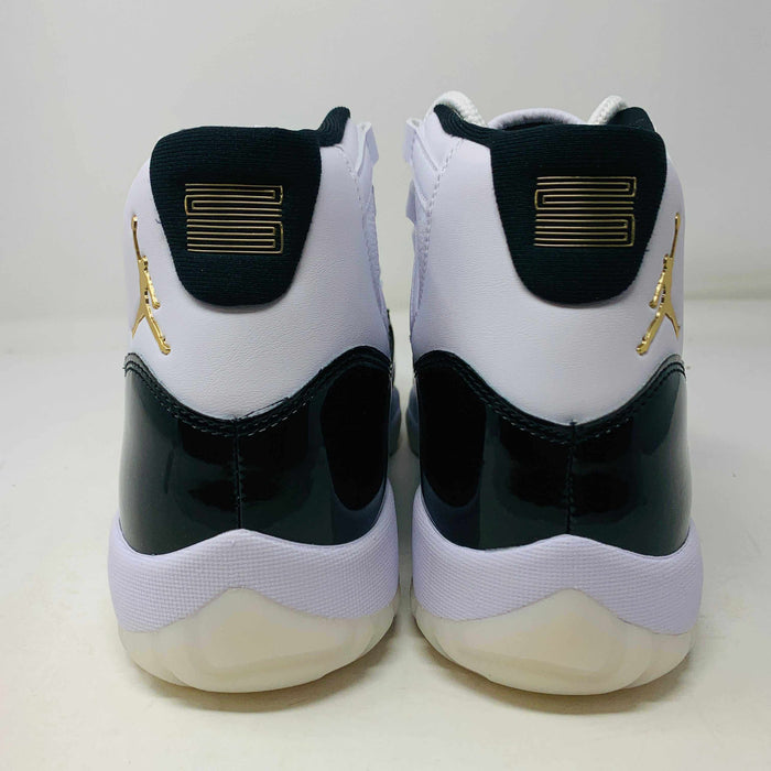 The Jordan 11 Retro DMP Gratitude (2023) features high-top sneakers in a white-black colorway with shiny accents. They have white laces, a crisp white midsole, and a translucent outsole, adorned with a small golden ankle logo and come in a sleek black box.