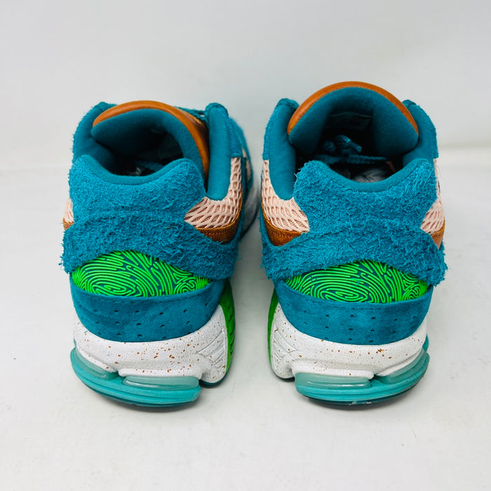 A pair of New Balance 2002R by Salehe Bembury, in colorful teal, pink, and green accents, sits atop a shoebox. Two extra lace sets—pink and green—are in front. The shoebox label details the size and style; the box is in good condition with a clean design.