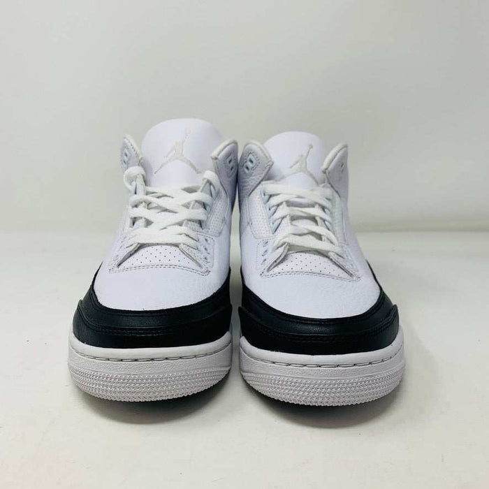 The Jordan 3 Fragment by Jordan, a white sneaker with black midsole and lime green heel detailing, is displayed on a closed blue shoebox.