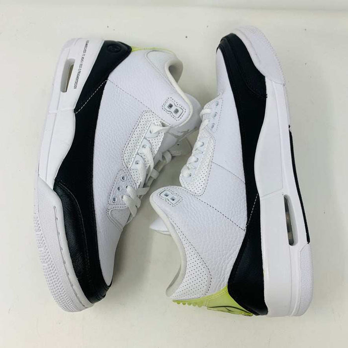 The Jordan 3 Fragment by Jordan, a white sneaker with black midsole and lime green heel detailing, is displayed on a closed blue shoebox.