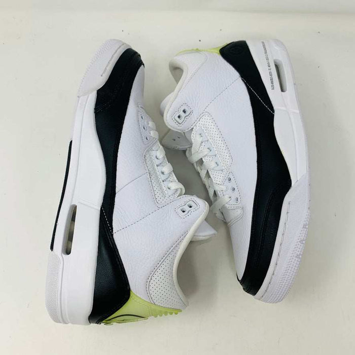 The Jordan 3 Fragment by Jordan, a white sneaker with black midsole and lime green heel detailing, is displayed on a closed blue shoebox.