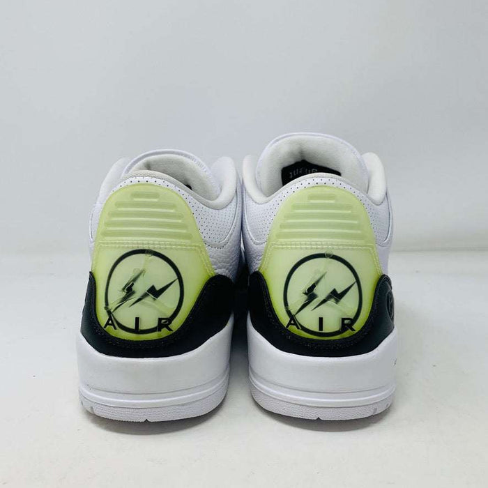 The Jordan 3 Fragment by Jordan, a white sneaker with black midsole and lime green heel detailing, is displayed on a closed blue shoebox.