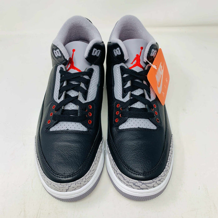 The Jordan 3 Retro OG Black Cement (2024) sneaker, featuring black and gray tones with red accents, is displayed on a sleek black shoebox. With textured details and visible air cushioning, an orange Nike Air tag authenticates this stylish addition to your collection.