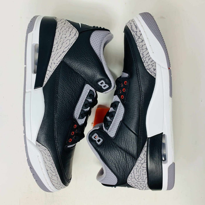 The Jordan 3 Retro OG Black Cement (2024) sneaker, featuring black and gray tones with red accents, is displayed on a sleek black shoebox. With textured details and visible air cushioning, an orange Nike Air tag authenticates this stylish addition to your collection.