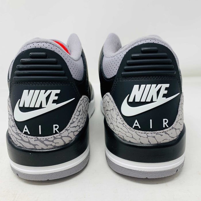 The Jordan 3 Retro OG Black Cement (2024) sneaker, featuring black and gray tones with red accents, is displayed on a sleek black shoebox. With textured details and visible air cushioning, an orange Nike Air tag authenticates this stylish addition to your collection.
