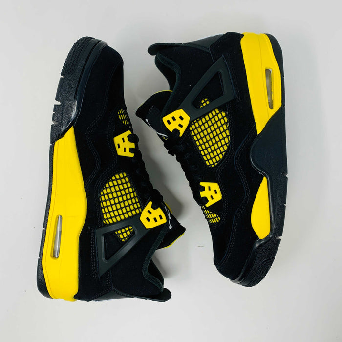 Brand new for 2023, the Jordan 4 Retro Thunder (GS) sneakers in black and yellow feature mesh panels and air cushioning. Positioned on a white background, they showcase their unique color scheme and design.
