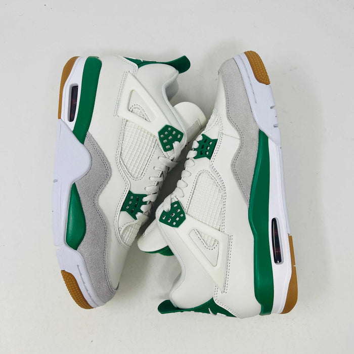 The Jordan 4 SB Pine Green sneakers, from the Jordan brand, are white with green accents and brown details. Featuring netted panels, green lace holders, and brown soles, they are displayed side by side on a white background.