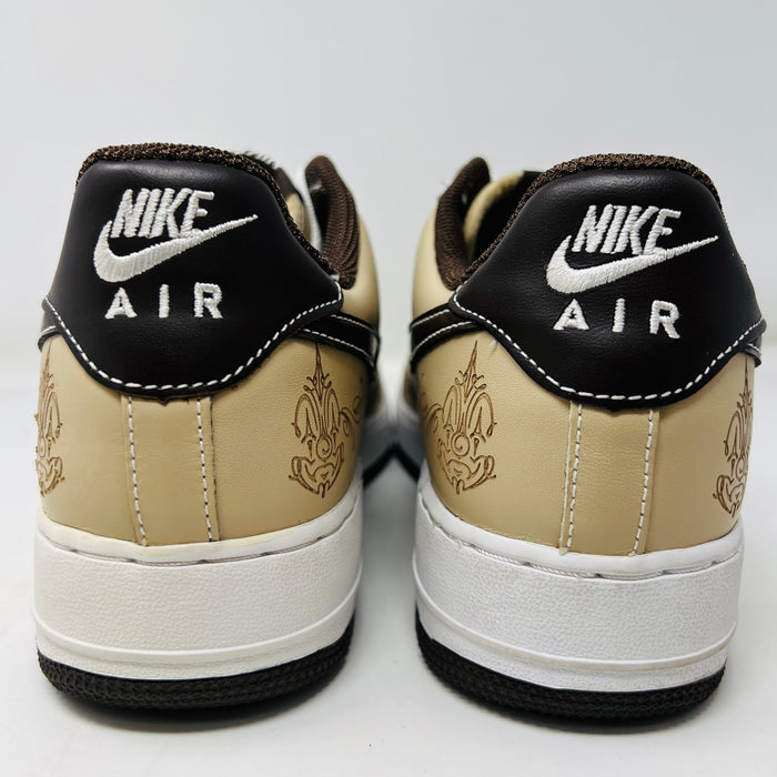 The Nike Air Force 1 Low Brown Pride sneakers feature beige and dark brown leather panels, white laces, and a white sole. They are shown from a top-down perspective in super clean condition on an immaculate white background.