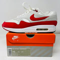 The Nike Air Max 1 Anniversary Red (2017/2018 Restock Pair) sneaker in white and red, features a visible air unit. It is showcased atop a pristine orange and gray box with a detailed label for size and specs, suitable for general wear.