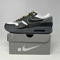 Nike Air Max 1 sneaker in black, white, and gray with yellow accents on gray Nike shoebox