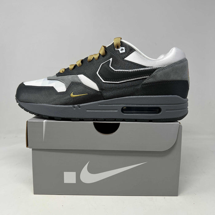 Nike Air Max 1 sneaker in black, white, and gray with yellow accents on gray Nike shoebox