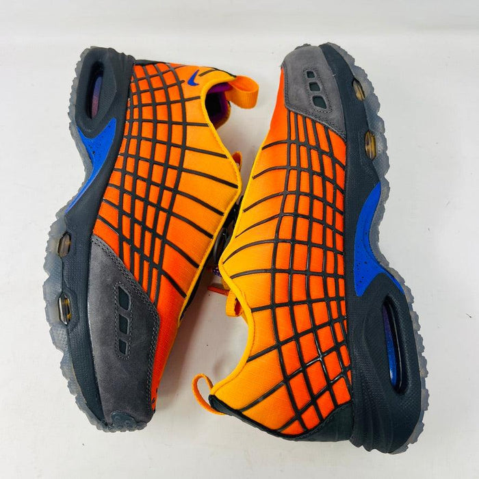 The Nike Air Max Sunder SP Kids of Immigrants Sunrise sneakers in bright orange and black feature a grid pattern with blue accents. An authentic swoosh and a circular K-I design mark the shoes and the orange box, highlighting their uniqueness.