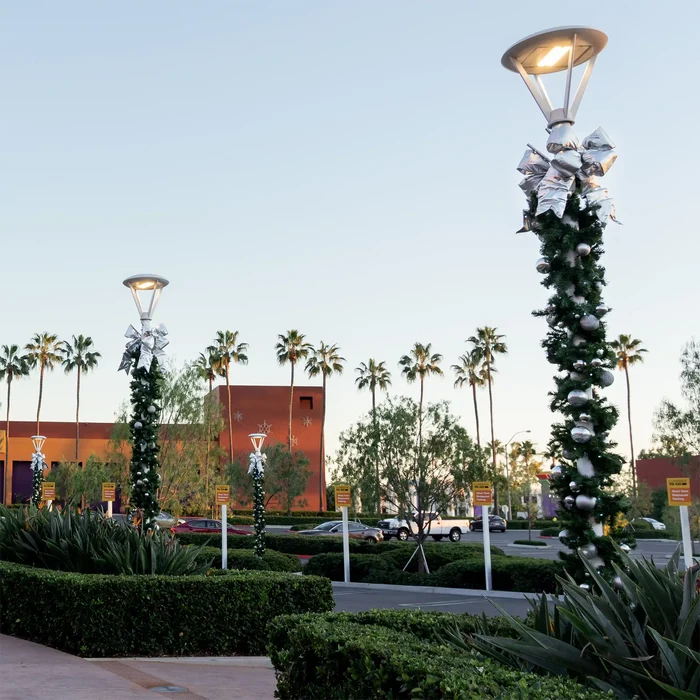 Decorative street lamp with greenery and silver bows in a parking lot with palm trees.