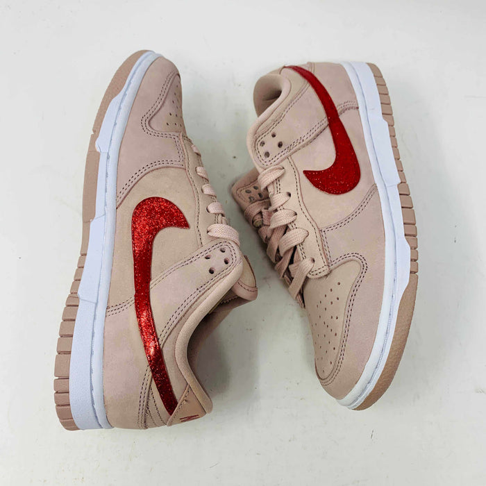 The Nike Dunk Low PRM Pink Oxford (W) Valentines Day CUSTOM sneakers feature a beige body, red glittery swoosh logos, white midsoles, and beige laces. Displayed against a white background, these sneakers highlight a stylish and sporty look.