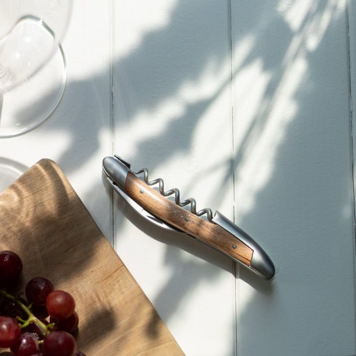 Forge de Laguiole Corkscrew, top-down view of satin steel and vine wood handle on white table.