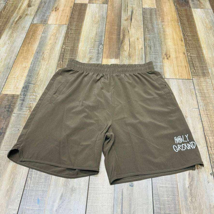 The Holy Ground Athletic Shorts (S24) feature a green design with Holy Ground printed in white on the lower left front, displayed on a wooden floor of brown and tan planks.
