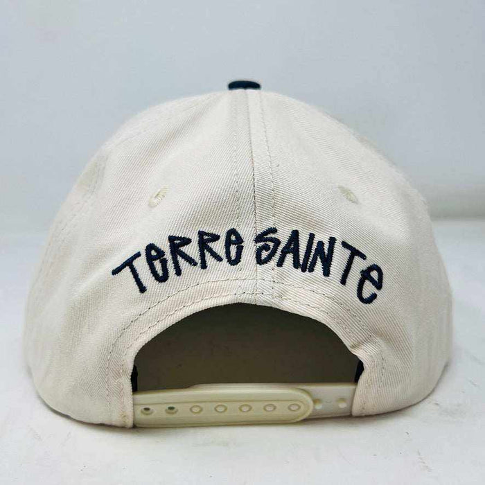 The Holy Ground Stussy Hat by Holy Ground is a streetwear accessory with HOLY GROUND embroidered in black on its white front panel, complemented by a green bill for a fresh touch.