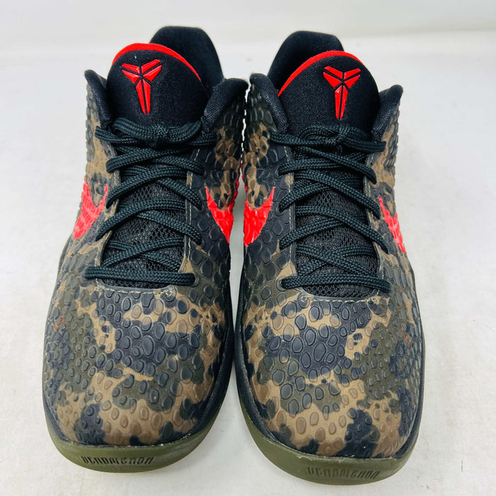 Close-up of a Nike Kobe 6 Protro Italian Camo (2024) (GS) shoe in black and dark olive with a red swoosh, resting on an orange Nike box. The 100% authentic shoe features a textured upper shown from the side, highlighting its design and striking color contrast.