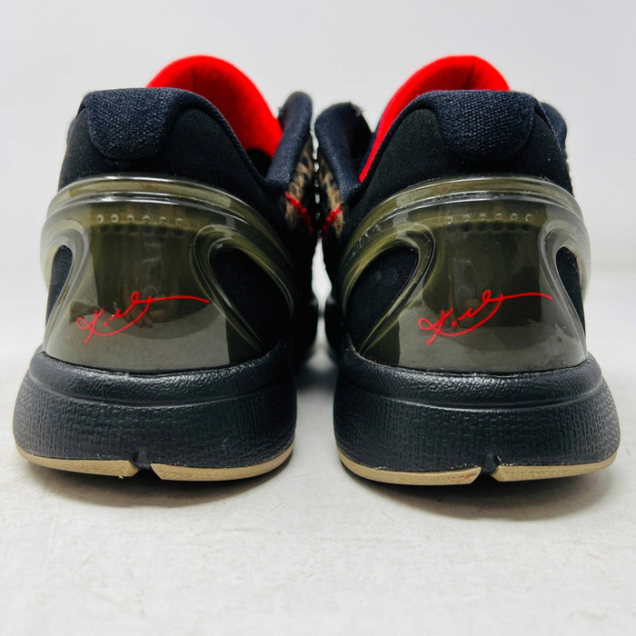 Close-up of a Nike Kobe 6 Protro Italian Camo (2024) (GS) shoe in black and dark olive with a red swoosh, resting on an orange Nike box. The 100% authentic shoe features a textured upper shown from the side, highlighting its design and striking color contrast.