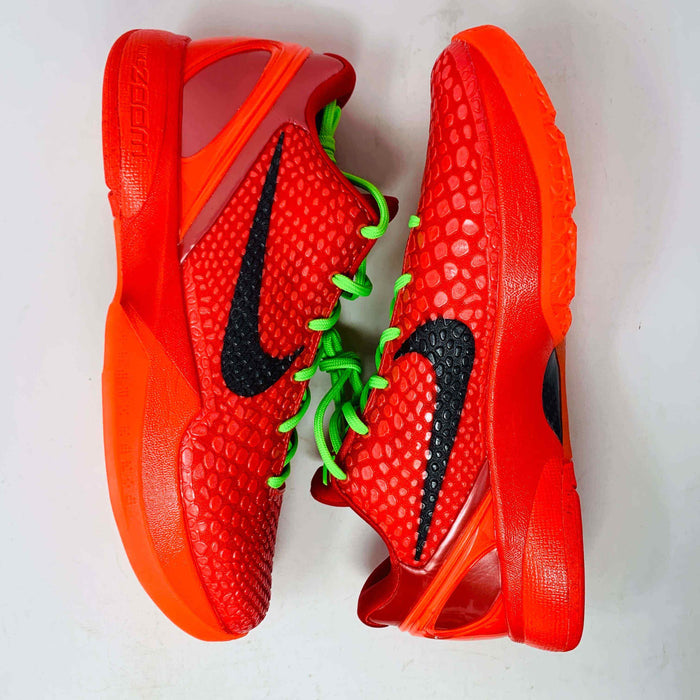 The Nike Kobe 6 Protro Reverse Grinch features a vibrant red colorway with black swoosh logos and bright green laces. Displayed on a white background, these athletic basketball shoes have soles and heel areas matching the bold red hue.