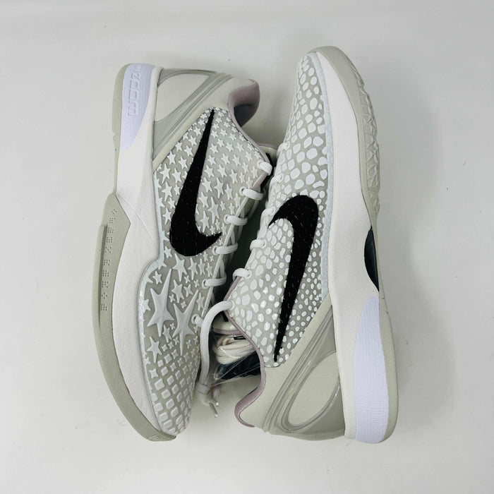 The Nike Kobe 6 Protro Sail All-Star shoes, featuring white textured patterns and black swoosh details with star designs, are elegantly displayed on a sleek black shoebox.