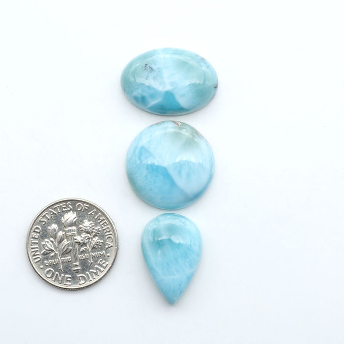Larimar stone cabochons, cut and polished, blue and white gemstones on a white background, with a US dime for scale