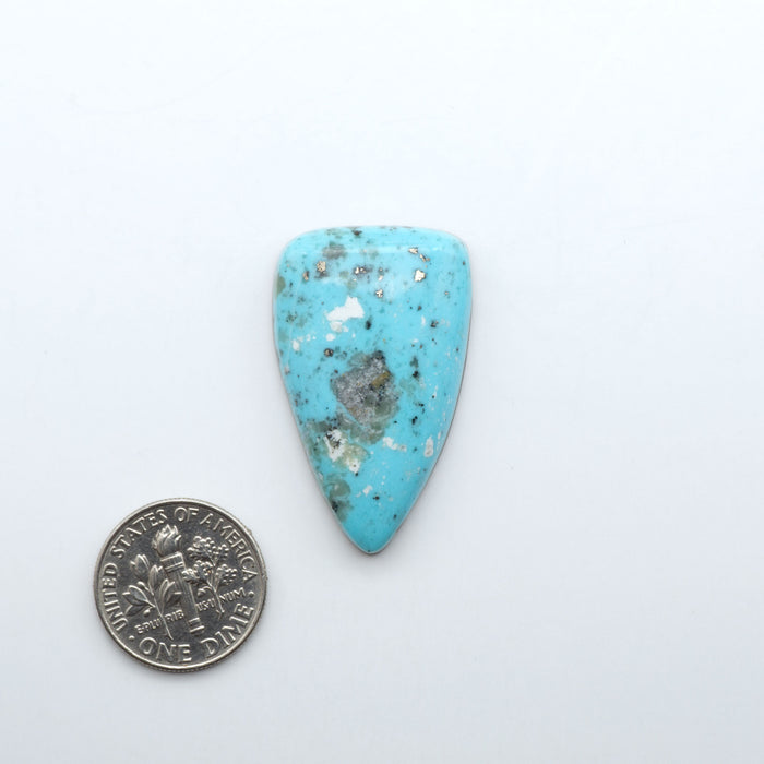 Nacozari Turquoise cabochons, blue to greenish-blue gemstones with black or brown matrix and pyrite on a white background, with a US dime for scale