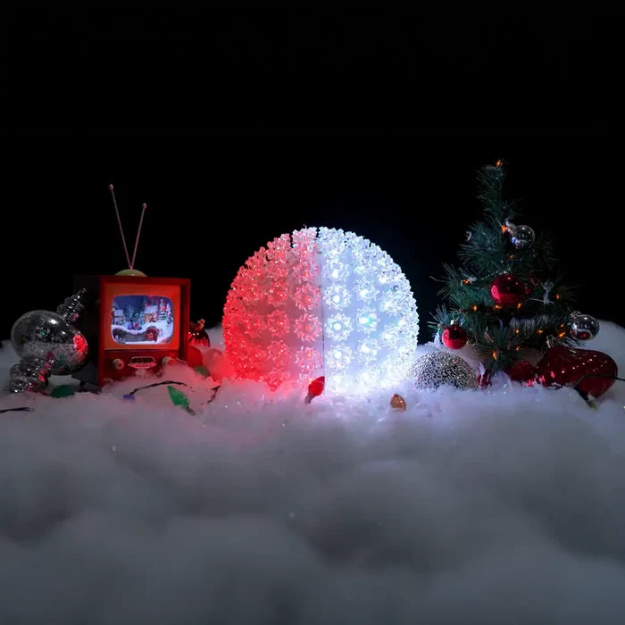 Decorative setup with a glowing orb, Christmas tree, and vintage TV in a snowy scene.