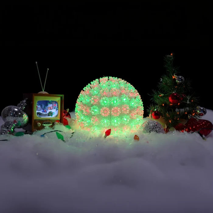 Decorative scene with a glowing green and red light ball, vintage TV, and Christmas tree in snow.