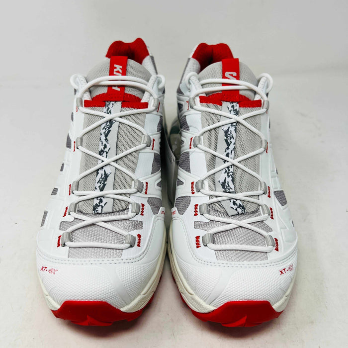 The Salomon XT-4K Kith Kithmas White Red sneakers rest on a black Kith box, with an extra laces bag. The shoes are 100% authentic, showcasing red accents and branding details.