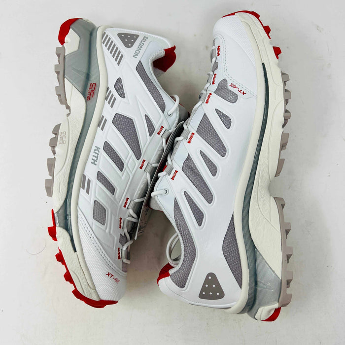 The Salomon XT-4K Kith Kithmas White Red sneakers rest on a black Kith box, with an extra laces bag. The shoes are 100% authentic, showcasing red accents and branding details.