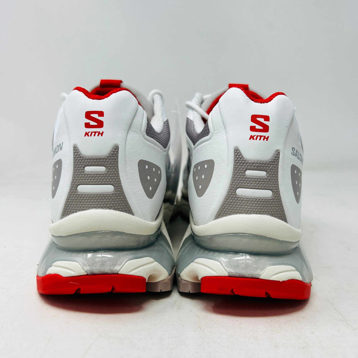 The Salomon XT-4K Kith Kithmas White Red sneakers rest on a black Kith box, with an extra laces bag. The shoes are 100% authentic, showcasing red accents and branding details.