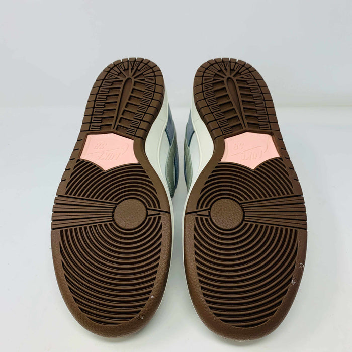 The Nike SB Dunk Low Yuto Horigome sneaker, with a white and light blue design featuring a gray swoosh, is displayed on a white Nike SB box. The authentic shoe has pink and brown laces, a brown sole, and an embroidered logo on the heel.