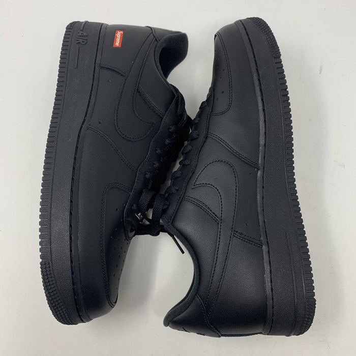The Nike Supreme Air Force 1 Black features a perforated design on the toe box, black supreme laces with a shiny tag, and a prominent Nike logo, all set against a plain white background.