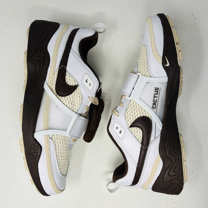 The Nike Zoom Field Jaxx Travis Scott Light Chocolate sneaker showcases a white and brown design with mesh and leather textures, Velcro strap, brown laces, and a prominent brown swoosh. It sits on a blue Nike shoebox.